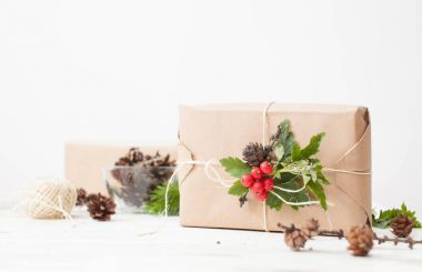 Holly ve çam kozalakları sapı ile düz kağıt sarılmış hediye