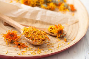 Bir tabloda bir tahta kaşık kuru calendula çiçeklenir