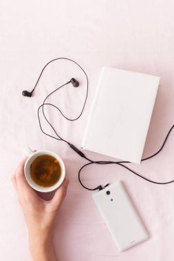 Elinde bir kitap ve müzik ile yatakta bitkisel çay