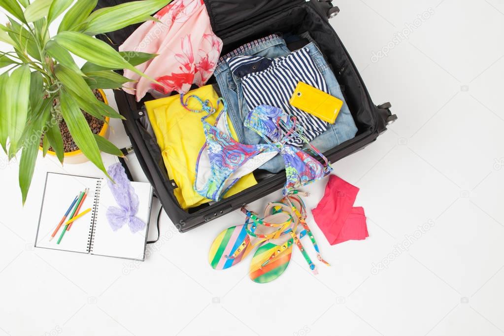 Open suitcase with summer things against a white background
