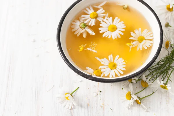 Fiori di camomilla infusi in una ciotola su un tavolo bianco — Foto Stock