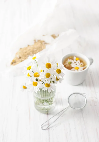 A bouquet of daisies and broth in a Cup on a white table — Stock Photo, Image