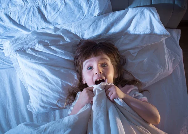 A menina está aterrorizada deitada na cama — Fotografia de Stock