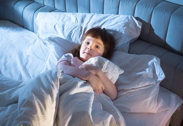 A menina está segurando uma colcha deitada na cama — Fotografia de Stock