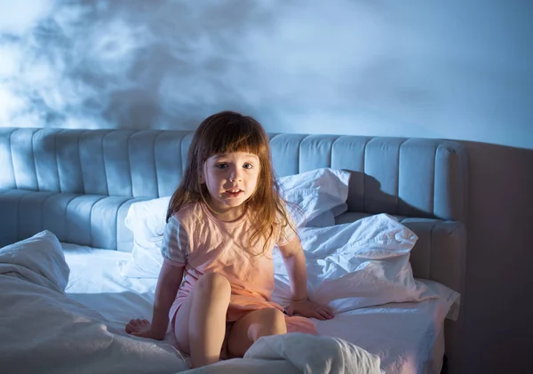Menina impertinente sentado na cama durante a noite — Fotografia de Stock