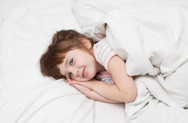 Een meisje van 4 jaar glimlachend in witte bed — Stockfoto