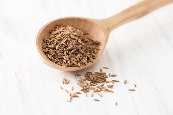 Cumin seeds in wooden spoon on white wooden table — Stock Photo, Image