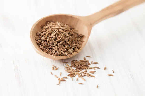 Semillas de comino en cuchara de madera sobre mesa de madera blanca — Foto de Stock