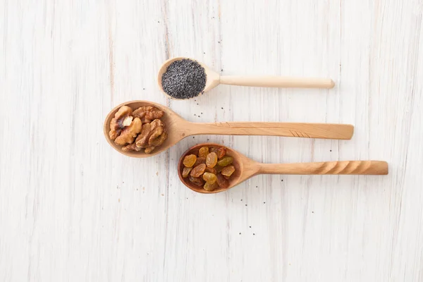 Pasas, nueces y semillas de amapola en cucharas de madera sobre blanco — Foto de Stock