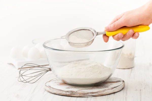 Peneirar farinha em uma xícara em uma mesa branca na cozinha — Fotografia de Stock