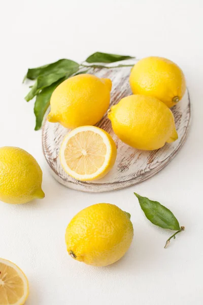 Ein Bund Zitronen mit Blättern und Zitronenscheiben auf weißem Betongrund. — Stockfoto