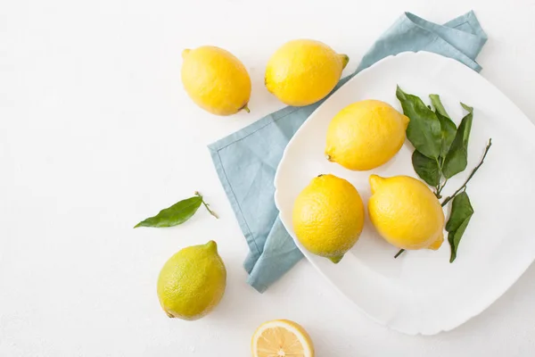 Un ramo de limones con hojas y limones en rodajas sobre un fondo de hormigón blanco . — Foto de Stock