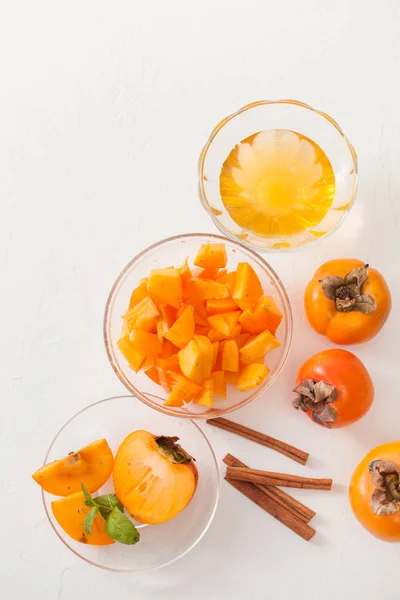 Chopped ripe persimmon in a bowl with cinnamon sticks on white table — Stock Photo, Image