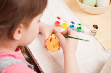 Kız evde masada yumurta boyalar