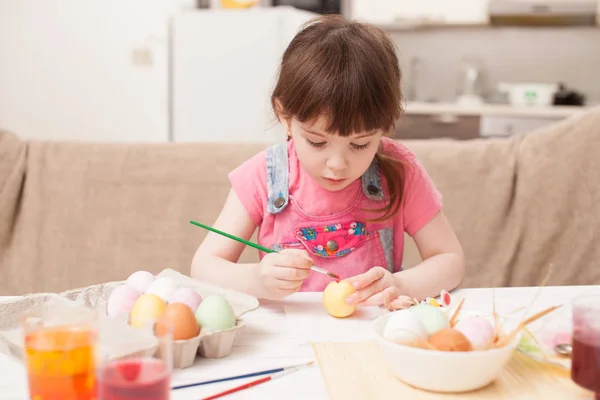 Het meisje schildert het ei aan de tafel thuis — Stockfoto