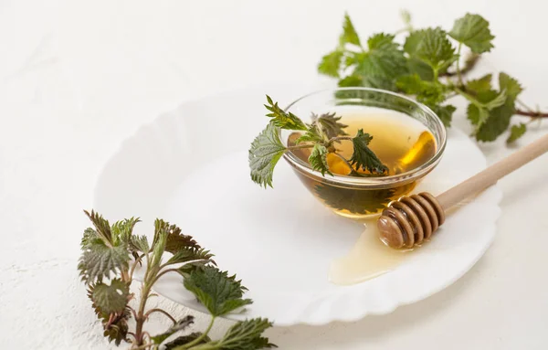 Corta la ortiga joven y el tazón de miel en un plato blanco — Foto de Stock