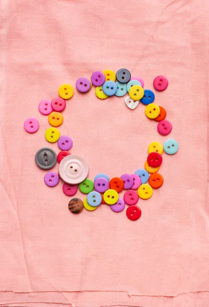 Tombol-tombol terang berwarna-warni dalam bentuk lingkaran pada kain merah muda terang — Stok Foto
