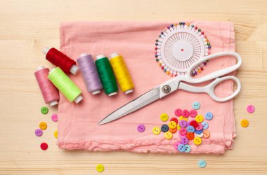 Dikiş iplikleri, iplikler, kumaş parçaları, ahşap masadaki düğmeler.