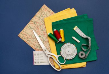 Koyu mavi arka planda dikiş aksesuarları olan kumaş parçaları.