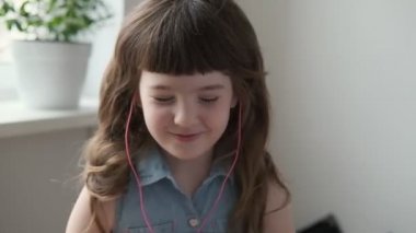 6-7 yaşlarında bir kız pembe kulaklıklarla müzik dinliyor ve evde dans ediyor.
