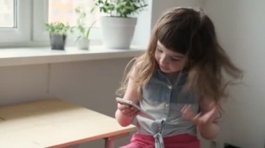 6-7 yaşlarındaki bir kız telefonunda kabarık saçlı komik özçekim fotoğrafları çekiyor ve sonuç karşısında şaşırıyor..