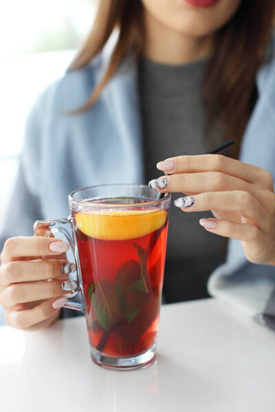 Руки молодой женщины, держащей чашку горячего мятного чая или горячего лимонада.
