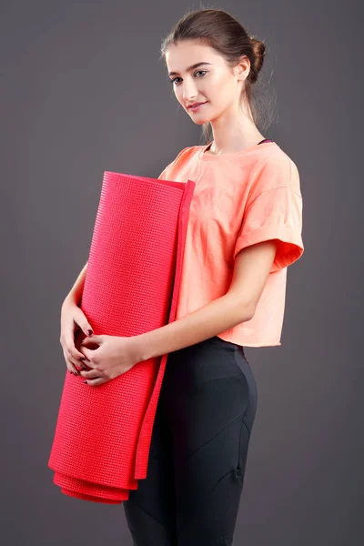 Junge attraktive Frau mit einer roten Yogamatte. isoliert auf schwarz — Stockfoto