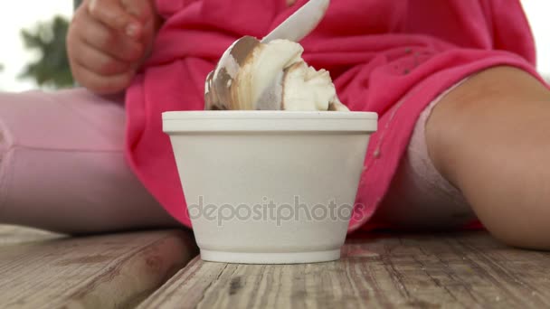 Dívka v růžovém jíst zmrzlinu na piknikový stůl — Stock video