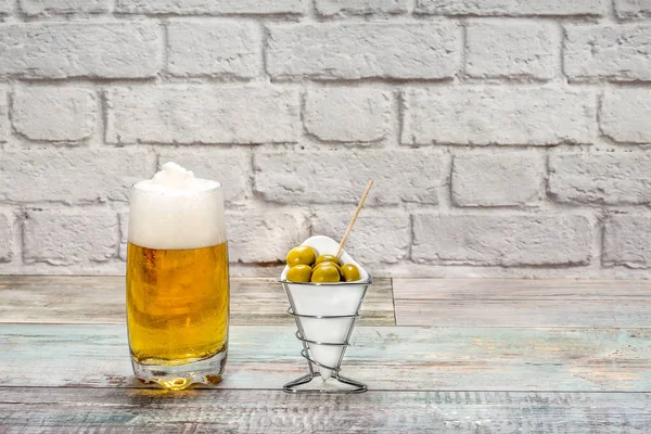 Vaso de cerveza con aceitunas verdes en una pared de ladrillo blanco — Foto de Stock