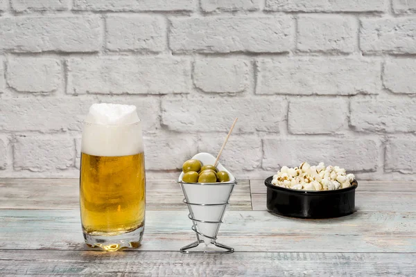 Vaso de cerveza con espuma y bol con aceitunas y palomitas de maíz — Foto de Stock