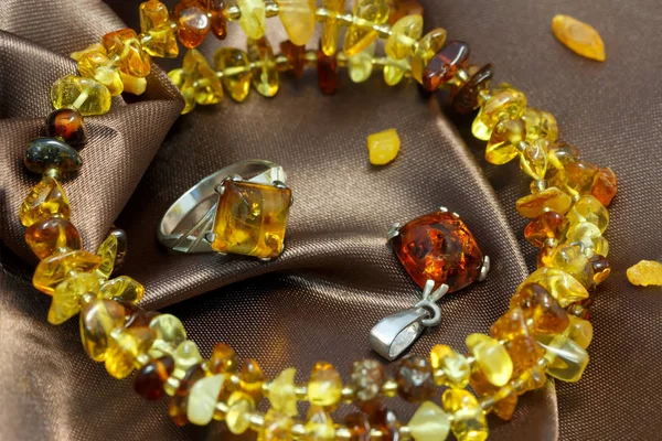 Closeup jewerly met authentieke natuurlijke Baltisch amber: armband, zilveren ring en hanger, aan bruin atlas — Stockfoto