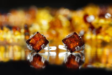 Closeup gümüş küpe rhombus otantik doğal Baltık Amber turuncu amber arka plan üzerinde siyah yüzeyi