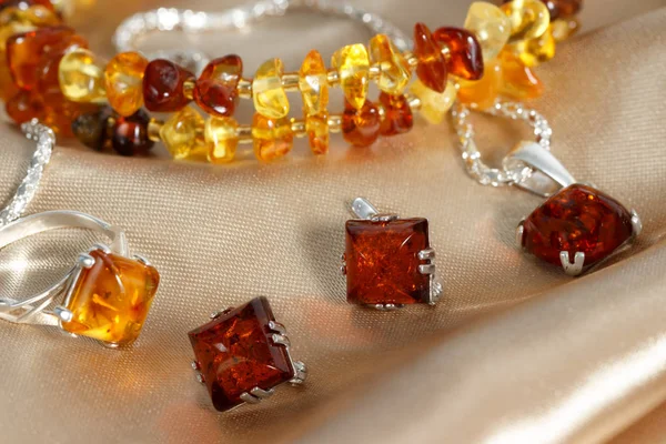 Closeup jewelry with  authentic  natural baltic amber : silver earrings, ring and pendant, on brown atlas surface. — Stock Photo, Image