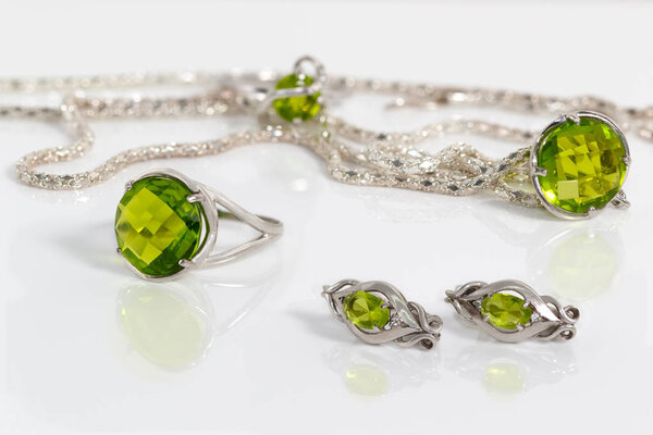 Close-up beauty silver earrings, ring and pendant with peridot on background chain and ring on white acrylic desk