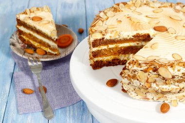 Vejetaryen havuçlu keki yakın plan mavi ahşap masadaki badem tezgahlı. Arka planda pastadan bir parça olan fincan tabağı..