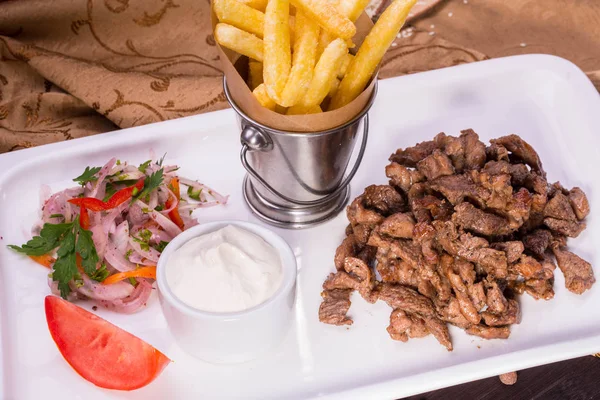 Pieces of braised beef with onions salad and sour cream sauce, is served with French fries