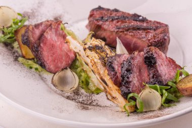 Sığır eti ve üstünlüğü, lahana ile bir ızgara sunulmaktadır bir ızgarada kızartılmış soğan, kızarmış patates ile marul yaprakları kırmızı şarap sos