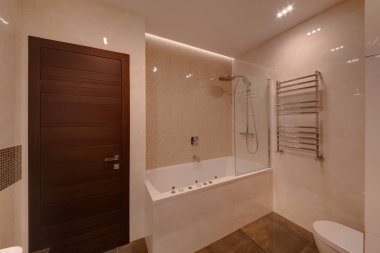 Dikdörtgen bir banyo ve duş, kahverengi bir kapı ve ışık duvarları ile bir banyo