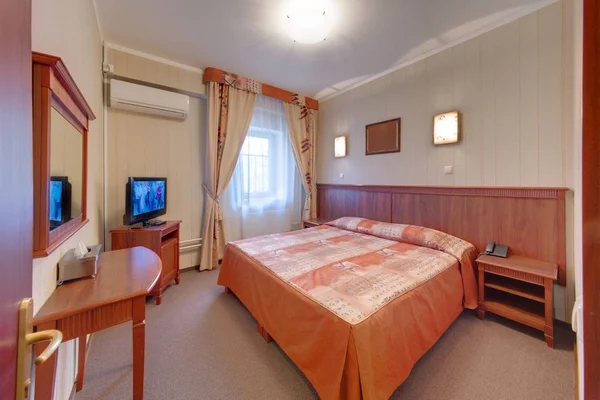 The bedroom with a big bed, the TV set and a dressing table on which there are napkins