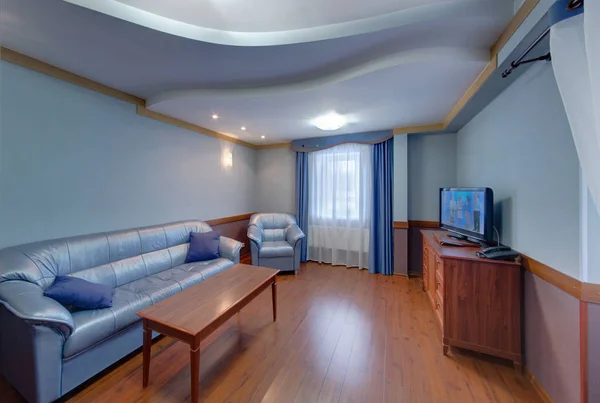 The blue room with upholstered furniture, a curbstone under the TV set and a coffee table