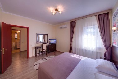 Hafif bir pencere ve karanlık perdeleri, tuvalet masasının ve ayna, Tv ve bir koridor görünümü ile yatak odası