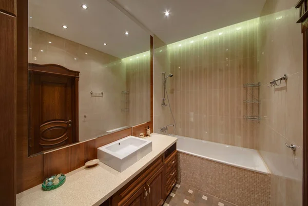 Bir banyo lavabo, büyük ayna, duş ve tuvalet aksesuarları altında karanlık mobilya ile