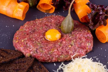 Bıldırcın yumurtalı et tartar, rendelenmiş peynir, çavdar ekmeği cipsi ve sebzeyle servis edilir.