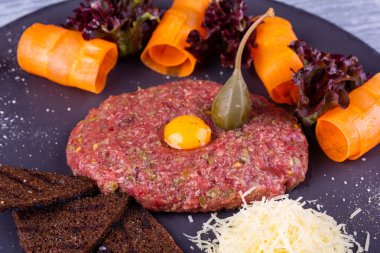 Bıldırcın yumurtalı et tartar, rendelenmiş peynir, çavdar ekmeği cipsi ve sebzeyle servis edilir.