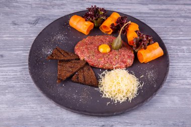 Bıldırcın yumurtalı et tartar, rendelenmiş peynir, çavdar ekmeği cipsi ve sebzeyle servis edilir.