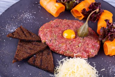 Bıldırcın yumurtalı et tartar, rendelenmiş peynir, çavdar ekmeği cipsi ve sebzeyle servis edilir.