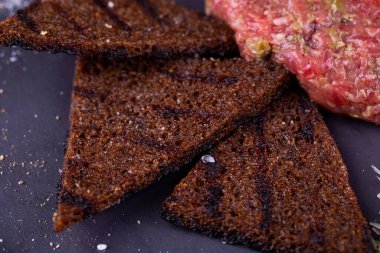 Bıldırcın yumurtalı et tartar, rendelenmiş peynir, çavdar ekmeği cipsi ve sebzeyle servis edilir.