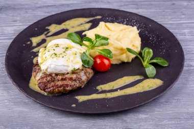 Yumurtalı bir parça biftek, patates püresi ve sebzeli vişneli domates.