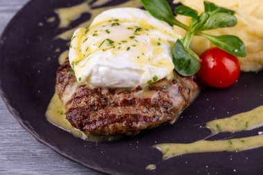 Yumurtalı bir parça biftek, patates püresi ve sebzeli vişneli domates.