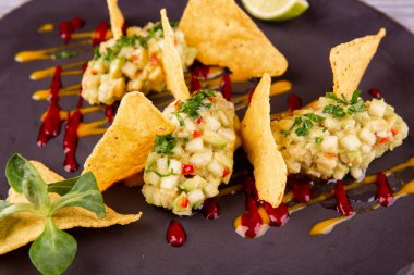 Avokado ve doğranmış sebzeli guacamole, cips, ketçap ve hardalla servis edilir.